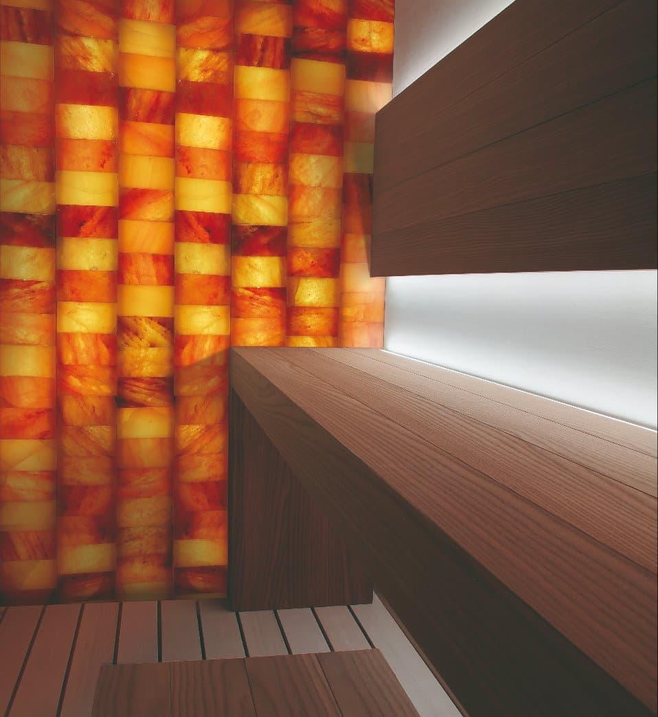 Warm backlit salt bricks beside timber Sauna benching