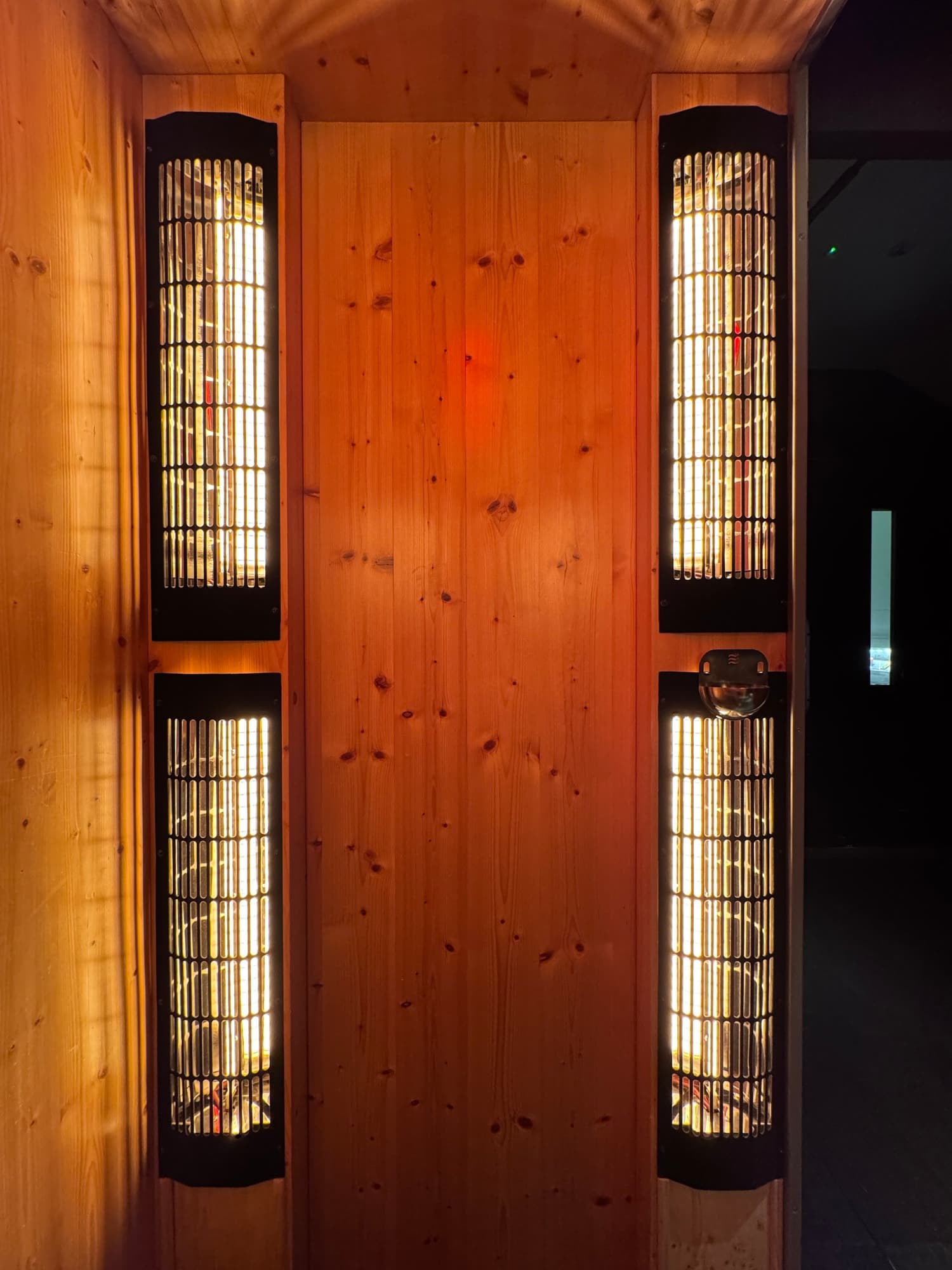 Two tall black light fixtures with vertical slats casting light onto a wooden wall in a dimly lit room.