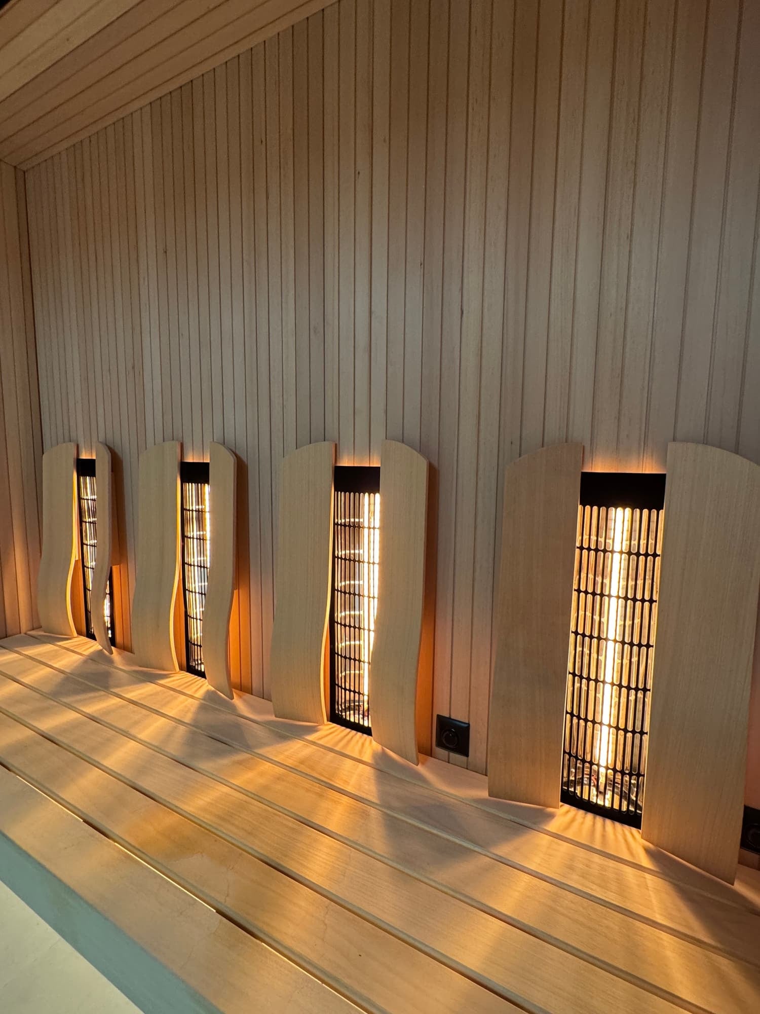 Interior of a Sauna with wooden walls, benches, and light fixtures emitting warm glow.
