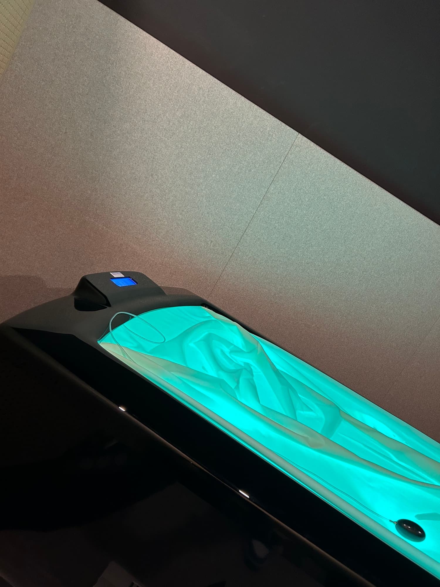 Illuminated touchscreen device with draped fabric inside a sleek, modern machine or container.