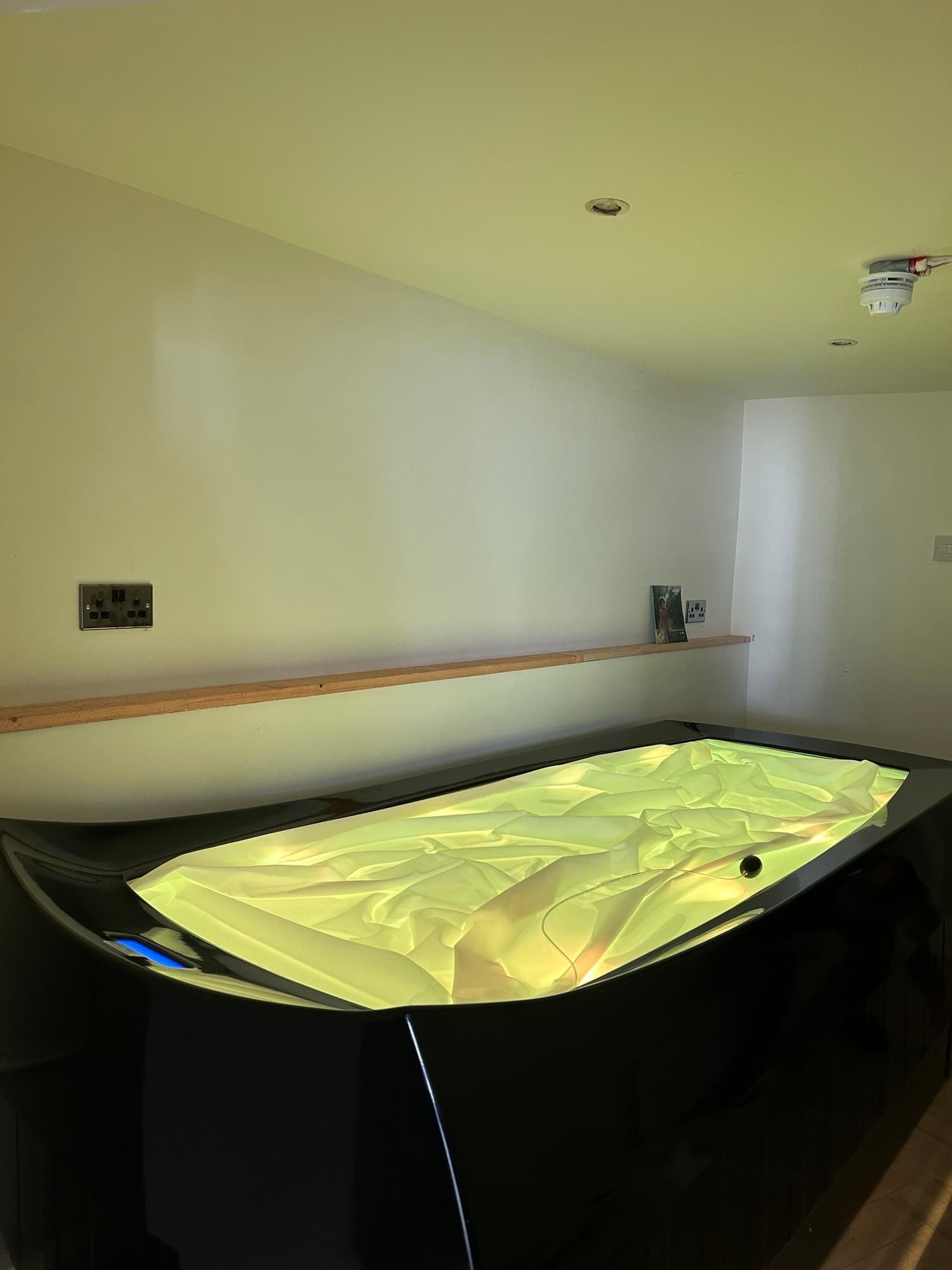 A futuristic gaming or entertainment pod with a glowing, crumpled yellow interior, set against a plain room with white walls and ceiling.